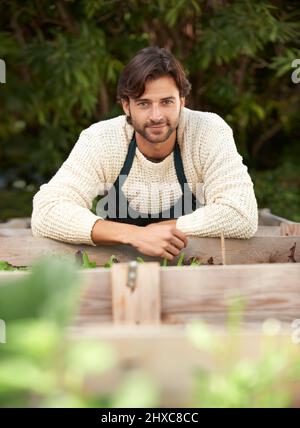 Gartenarbeit ist eine Leidenschaft. Porträt eines hübschen jungen Gärtners, der sich auf seine Pflanzenkästen stützt. Stockfoto