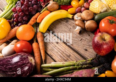 Blick aus der Höhe auf verschiedene Gemüse und Früchte mit leerer Herzform auf Holztisch Stockfoto