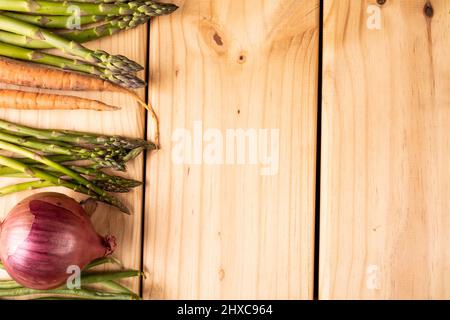 Blick von oben auf Spargel mit Karotten und Zwiebeln auf Holztisch mit leerem Raum Stockfoto