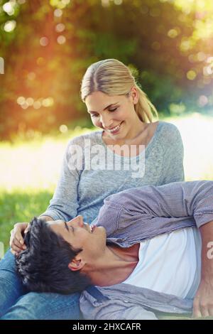 Die Liebe fiel ihr einfach in den Schoß. Aufnahme eines glücklichen jungen Paares, das auf dem Gras liegt und einen liebevollen Moment miteinander teilt. Stockfoto