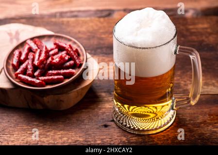 Ein Glas Bier und Snacks - getrocknete Würstchen auf einem Holzhintergrund. Stockfoto