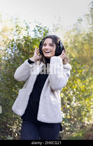 Junge Frau mit Kopfhörern, die im Wald zu Musik tanzt Stockfoto