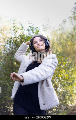 Junge Frau mit Kopfhörern, die im Wald zu Musik tanzt Stockfoto