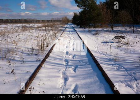 Verschneite alte ungenutzte Bahnstrecken im Winter, Fußabdrücke im Schnee Stockfoto