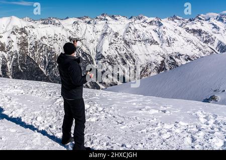 Drohne, die im Winter von der männlichen Hand auf dem Gipfel des verschneiten Berges abheben Stockfoto