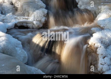 Ein schnell fließender Bach, der im Winter von Eis und Schnee umgeben ist, Torup, Halland, Schweden Stockfoto