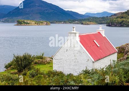 Eine kleine Croft mit einem roten Wellblechdach am Ufer des Loch Shieldaig in Ardheslaig, Highland, Schottland, Großbritannien. Stockfoto