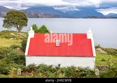 Eine kleine Croft mit einem roten Wellblechdach am Ufer des Loch Shieldaig in Ardheslaig, Highland, Schottland, Großbritannien. Stockfoto