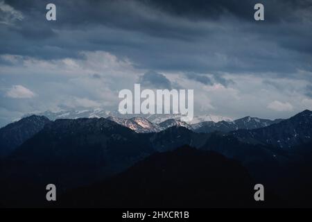 Landcsape Bild von fernen Bergen mit Gipfeln teilweise mit Schnee bedeckt unter bewölkten Bedingungen während des Sonnenuntergangs Stockfoto