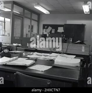 1958, historische Ansicht eines leeren Verwaltungsbüros und eines Industriegeländes, zeigt einen Papierkram, Lieferscheine und Akten auf einem Schreibtisch, mehrere Einwählbakerlite-Telefone der Ära und Aktenschränke aus Metall. Auf dem Schreibtisch, Port Talbot, Wales, befindet sich ein Aschenbecher mit Double Diamond-Schriftzug. Stockfoto