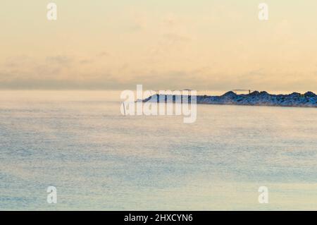 Minimaler Blick auf das Meer von der Küste Helsinkis. Das Wetter ist so kalt, dass das Wasser gefriert und einen leichten Nebel auf seine Oberfläche versprüht Stockfoto