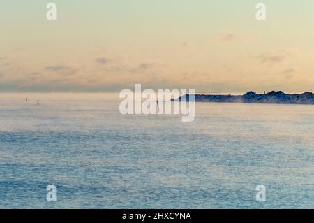 Minimaler Blick auf das Meer von der Küste Helsinkis. Das Wetter ist so kalt, dass das Wasser gefriert und einen leichten Nebel auf seine Oberfläche versprüht Stockfoto