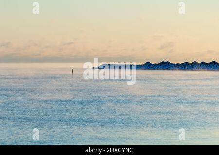 Minimaler Blick auf das Meer von der Küste Helsinkis. Das Wetter ist so kalt, dass das Wasser gefriert und einen leichten Nebel auf seine Oberfläche versprüht Stockfoto