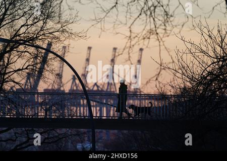 Hamburg, Deutschland. 11.. März 2022. Eine Frau mit einem Hund geht im Sonnenuntergang über eine Brücke. Kredit: Marcus Brandt/dpa/Alamy Live Nachrichten Stockfoto