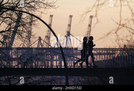 Hamburg, Deutschland. 11. März 2022. Joggingweibchen, die im Sonnenuntergang über eine Brücke laufen. Kredit: Marcus Brandt/dpa/Alamy Live Nachrichten Stockfoto