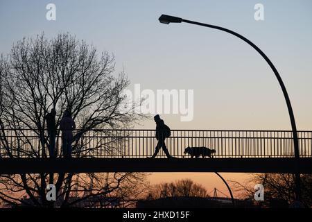 Hamburg, Deutschland. 11. März 2022. Passanten gehen im Sonnenuntergang über eine Brücke. Kredit: Marcus Brandt/dpa/Alamy Live Nachrichten Stockfoto