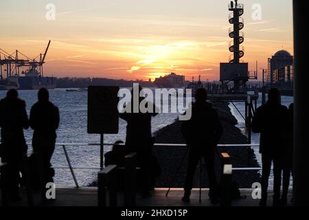 Hamburg, Deutschland. 11. März 2022. Passanten genießen den Sonnenuntergang im Hafengebiet an der Elbe im Hamburger Hafen. Kredit: Marcus Brandt/dpa/Alamy Live Nachrichten Stockfoto