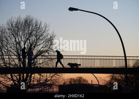 Hamburg, Deutschland. 11. März 2022. Passanten gehen im Sonnenuntergang über eine Brücke. Kredit: Marcus Brandt/dpa/Alamy Live Nachrichten Stockfoto