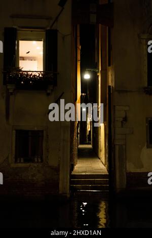 Enge beleuchtete Gasse direkt am Kanal in der Altstadt von Venedig, Italien Stockfoto