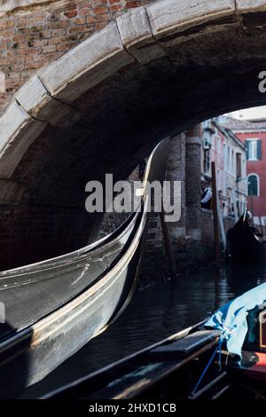 Venezianische Gondeln segeln unter einer schmalen Brücke auf einem kleinen Kanal in Venedig, Italien Stockfoto