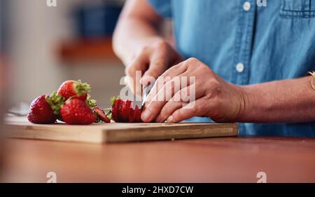 Jeder Obstsalat braucht Erdbeeren. Ausschnitt einer nicht erkennbaren älteren Frau, die beim Zubereiten des Frühstücks in ihrer Küche Erdbeeren zerschnitt Stockfoto
