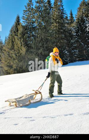 Junge Frau auf Winterwanderung bei Mittenwald, Schlitten vor Bergkulisse im Schnee, Bayern, Oberbayern, Deutschland, Urlaub, Winter, Stockfoto