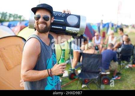 Mit meiner Boombox rocken. Aufnahme eines Mannes, der eine Boom-Box auf seiner Schulter trägt und bei einem Musikfestival im Freien ein Bier trinkt. Stockfoto