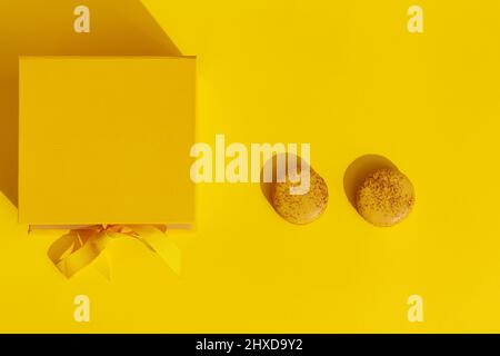 Gelbe Geschenkbox mit Schleife und zwei französischen Makronen auf gelbem Hintergrund. Gruß zum Internationalen Frauentag am 8. März, Muttertag, geburtet Stockfoto