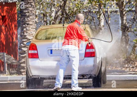 Ein nicht identifizierter Mann reinigt sein Auto mit einem Hochdruckwasser an der Tankstelle Stockfoto