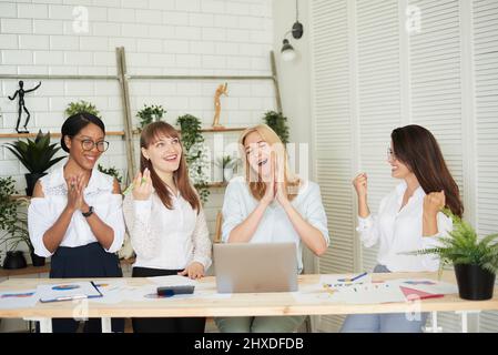 Emotionale Geschäftsfrauen, multiethnische Unternehmensmitglieder brüllen vor Freude, fühlen sich glücklich, erreichen Geschäftsziel, unterzeichnen wichtigen Vertrag, realisieren würdige Projekt Stockfoto