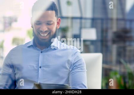 Es freut mich, dass mein Unternehmen abbricht. Eine kleine Aufnahme eines hübschen jungen Geschäftsmannes, der allein in seinem Büro sitzt und ein digitales Tablet verwendet. Stockfoto