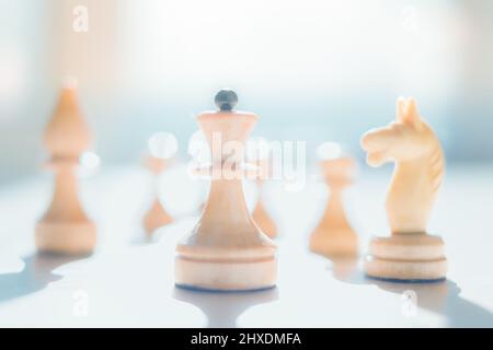 Silhouetten von Schachfiguren, die in Sonnenlicht getaucht sind. Das Bild befindet sich in einer hohen Taste. Die Schachkönigin führt die Krieger an. Abstraktion der Kampfstrategie. Bu Stockfoto