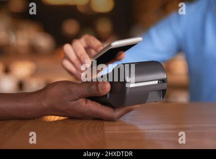 Tippen Sie auf, um zu bezahlen. Kurzer Schuss einer unkenntlichen Frau, die in einem Café bezahlt. Stockfoto