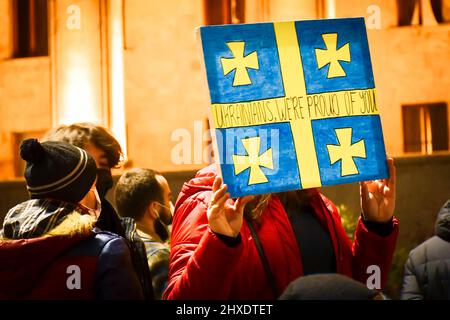 Tiflis, Georgien - 1.. märz 2022: Frau hält und zeigt handgemachtes Gemälde der ukrainischen Flagge mit dem Titel "Ukrainer wir sind stolz auf dich" Stockfoto