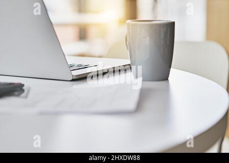 Am frühen Morgen im Büro. Nahaufnahme eines Laptops und einer Kaffeetasse auf einem Schreibtisch. Stockfoto