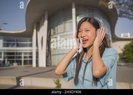 Junge schöne asiatische Mädchen mit Kopfhörern glücklich lächeln und tanzen auf der Straße. Stockfoto