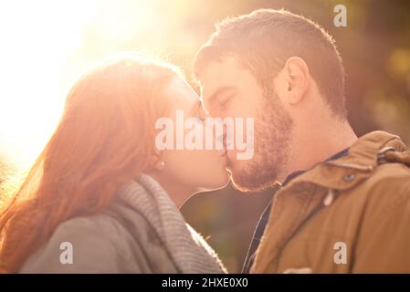 Dieser Kuss, der deine Seele erleuchtet. Aufnahme eines glücklichen jungen Paares, das sich im Freien einen Kuss teilt. Stockfoto