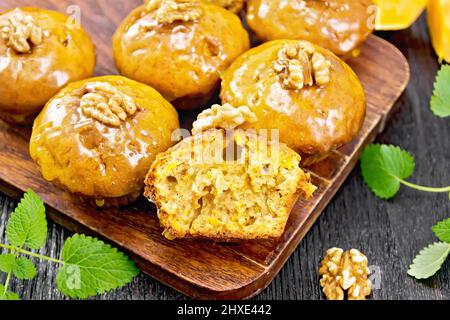 Kleine Kürbis-Cupcakes mit orangefarbener Glasur und Walnüssen, Minze-Zweige auf Holzbrett-Hintergrund Stockfoto