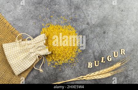 Bulgur, Getreide aus gekochtem, getrocknetem und zerkleinertem Weizen. Getreide aus einer Tüte auf dunklem Hintergrund gegossen Stockfoto