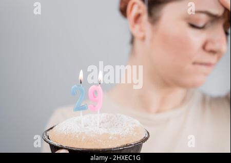 Unglückliche Frau hält einen Kuchen mit Kerzen für ihren 29. Geburtstag. Das Mädchen weint über den Verlust der Jugend. Stockfoto