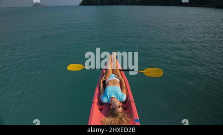 Die ziemlich schlanke Frau im eleganten Badeanzug liegt im rosa Plastikkajak, das auf dem azurblauen Ozean in der exotischen Urlaubsoberansicht driftet. Reisen in tropische Länder. Stockfoto