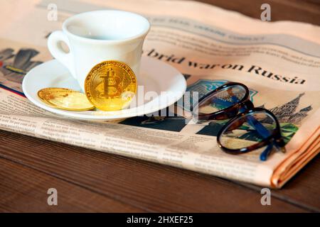 New York NY USA - März 06. 2022: Morgendliche Bitcoin-Krypto-Währung, eine Tasse leckeren Kaffee und Zeitungen berichten über die Invasion der Ukra in den vergangenen Nächten Stockfoto