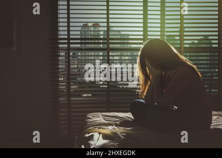 Depressive Frauen sitzen Kopf in den Händen auf dem Bett im dunklen Schlafzimmer mit wenig Licht Umgebung, dramatische Konzept Stockfoto