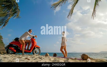 Motorroller Road Trip. Schönes Paar auf rotem Motorrad in weißen Kleidern am Sandstrand. Hochzeit gerade verheiratete Menschen, die in der Nähe von tropischen Palmen, Meer. Ho Stockfoto