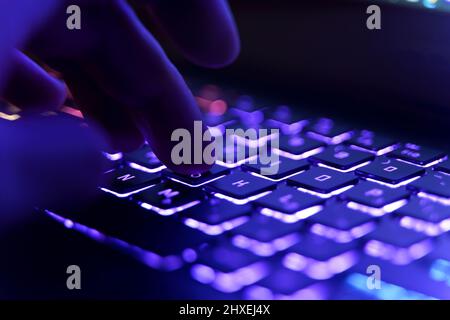 Arbeiten an einer Neon-Computertastatur mit farbiger Hintergrundbeleuchtung. Computer-Videospiele, Hacking, Technologie, Internet-Konzept. Ausgewählter Fokus. Hochwertige Fotos Stockfoto