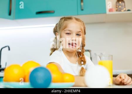 Ein kleines Mädchen von 7-8 Jahren verzerrt ihr Gesicht, nachdem es frisch gepressten Orangensaft getrunken hat. Babyemotionen Stockfoto