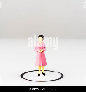 Ein Miniaturmodell einer Frau, isoliert in einem Kreis, der auf einer Oberfläche gezeichnet ist Stockfoto