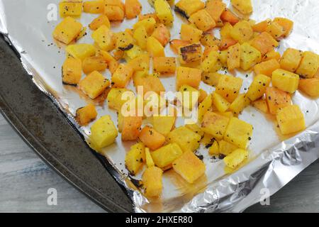 Geröstete Butternut-Squashwürfel mit Gewürzen auf aluminiumfoliengesäumtem Backblech Stockfoto