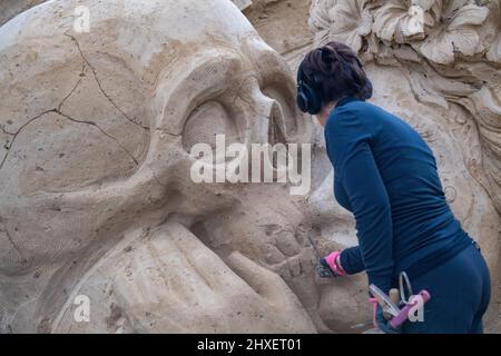 Binz, Deutschland. 11. März 2022. Eine Frau arbeitet an einer Sandskulptur der Sandskulptur-Show 'What a wonderful world'. Die Skulpturen zeigen Landschaften, Menschen und Fabelwesen. Quelle: Stefan Sauer/dpa/Alamy Live News Stockfoto