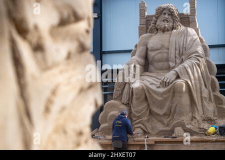 Binz, Deutschland. 11. März 2022. Ein Mann arbeitet an einer Sandskulptur von Zeus, dem Vater der Götter, in der Sandskulptur-Show "What a wonderful world". Die Skulpturen zeigen Landschaften, Menschen und Fabelwesen. Quelle: Stefan Sauer/dpa/Alamy Live News Stockfoto